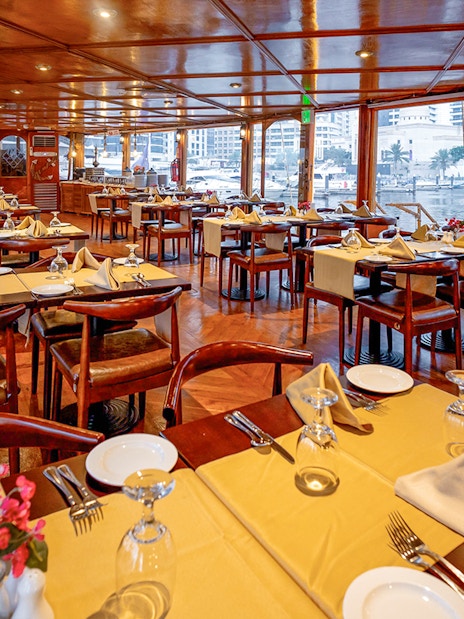 Dining setup on Alexandra Dhow Cruise in Dubai Marina with tables and city view.