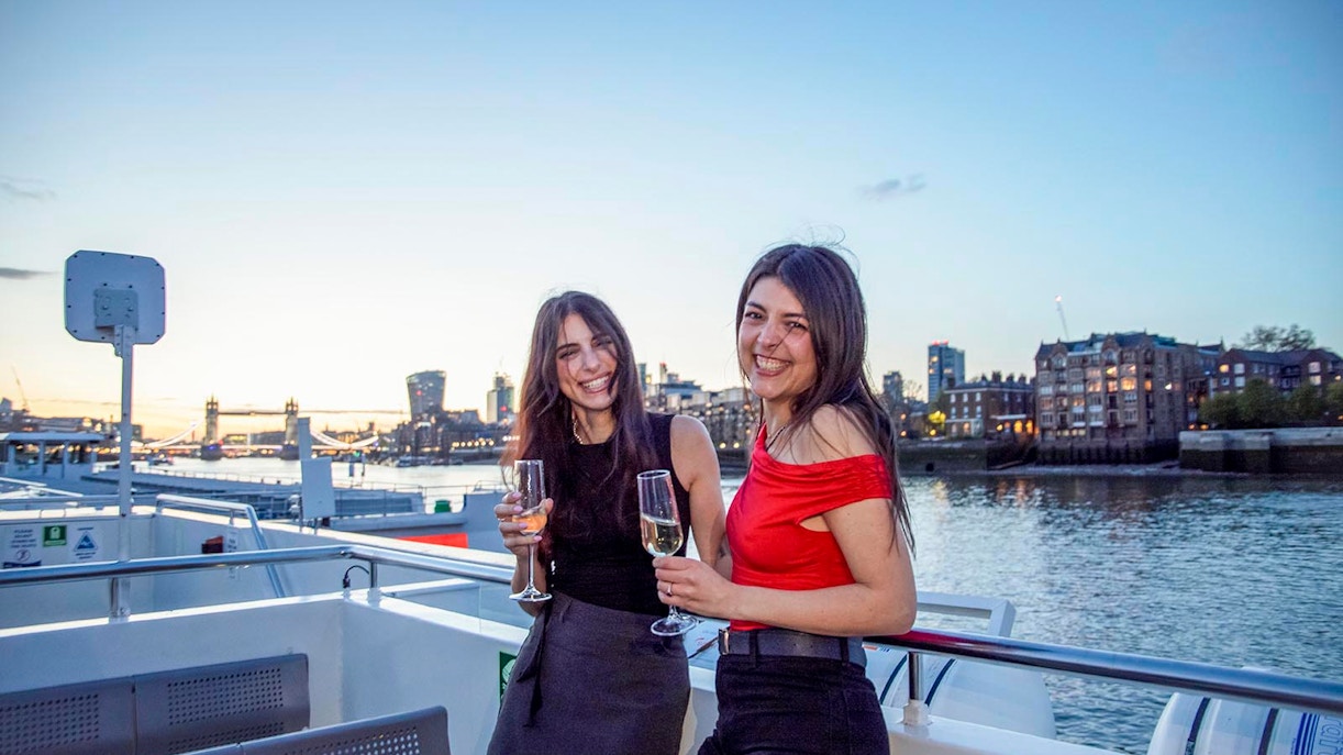 Guests enjoying drinks on a boat deck with a view of Tower Bridge, London.