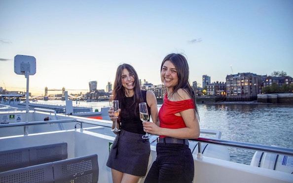 Guests enjoying drinks on a boat deck with a view of Tower Bridge, London.