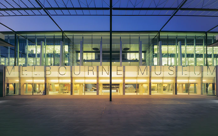 Melbourne Museum entrance illuminated at dusk, showcasing modern architecture.