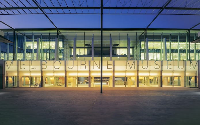 Melbourne Museum entrance illuminated at dusk, showcasing modern architecture.