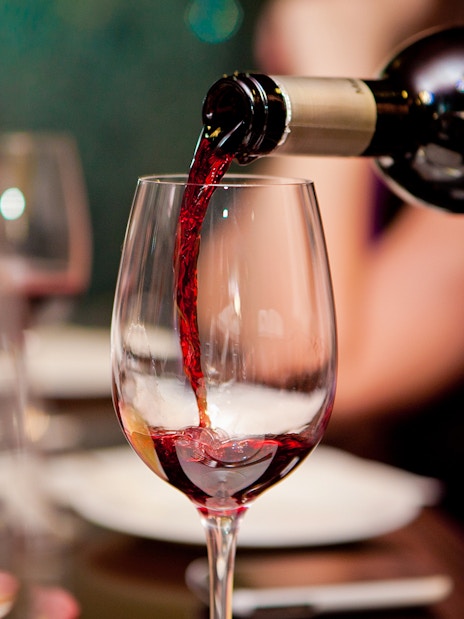 Red wine being poured into a glass at a restaurant table.