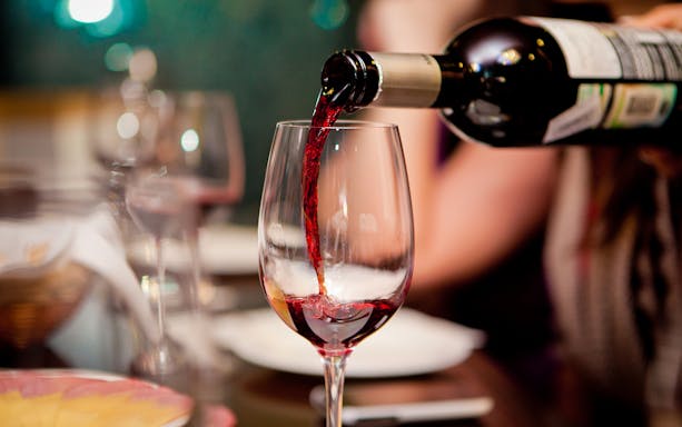 Red wine being poured into a glass at a restaurant table.