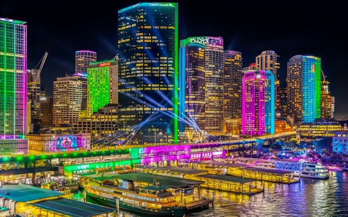 Sydney Harbour illuminated during Vivid Lights Cruise with colorful skyscrapers and boats.