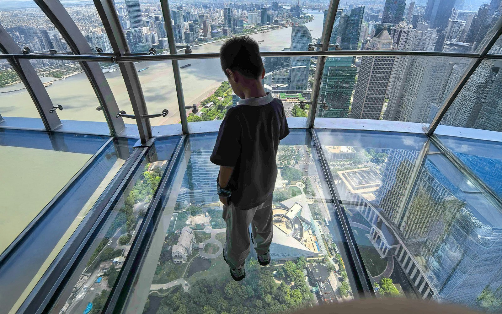 Child on transparent skywalk at Oriental Pearl Tower, Shanghai, overlooking cityscape.