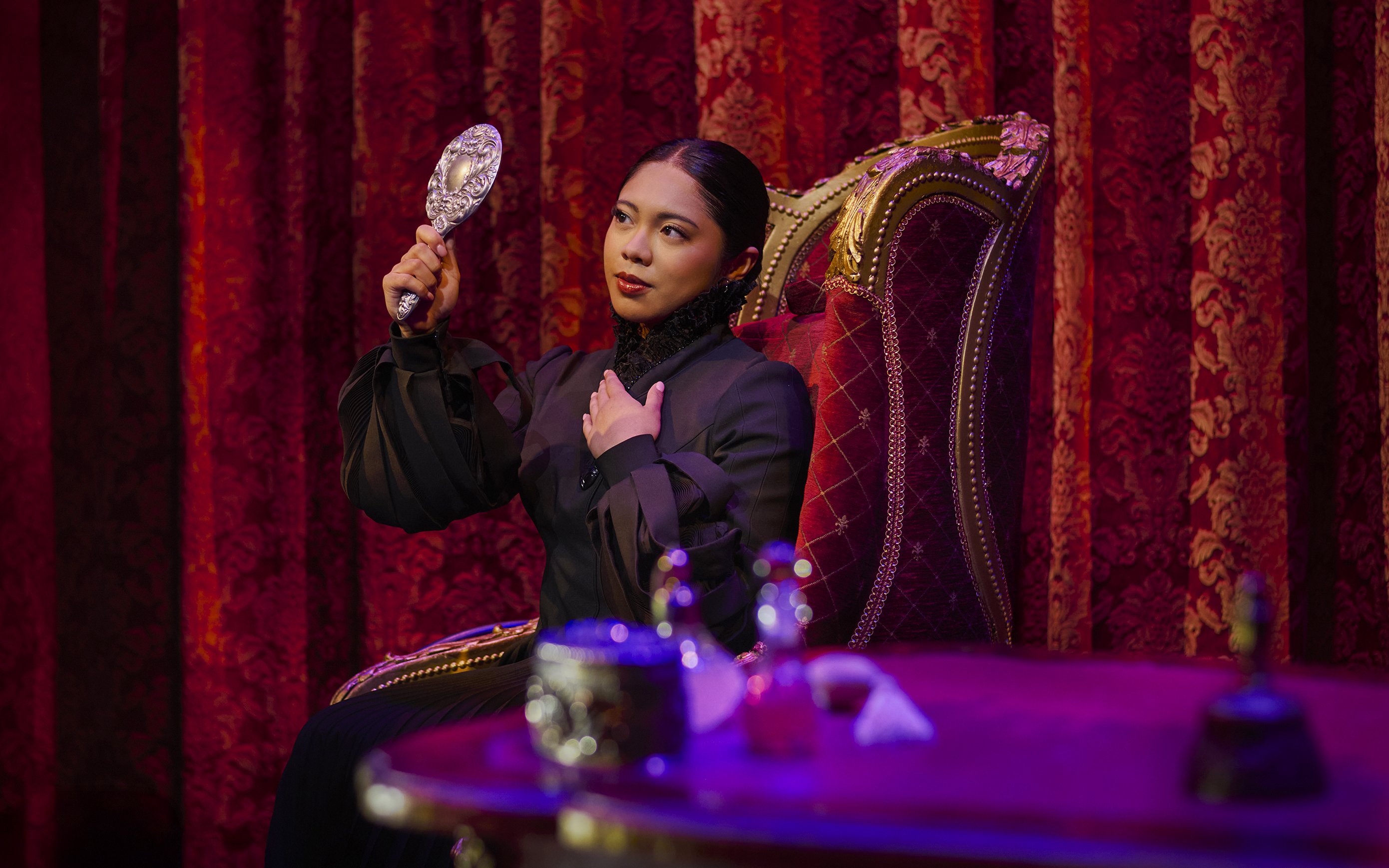 Performer in costume holding a mirror on stage during a scene from Wicked.