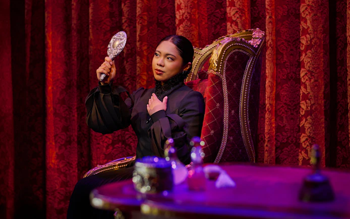 Performer in costume holding a mirror on stage during a scene from Wicked.