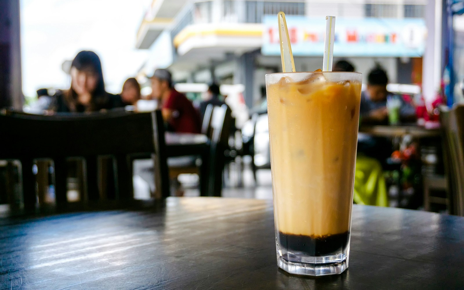 Iced Teh C peng on a cafe table in a bustling Malaysian eatery.