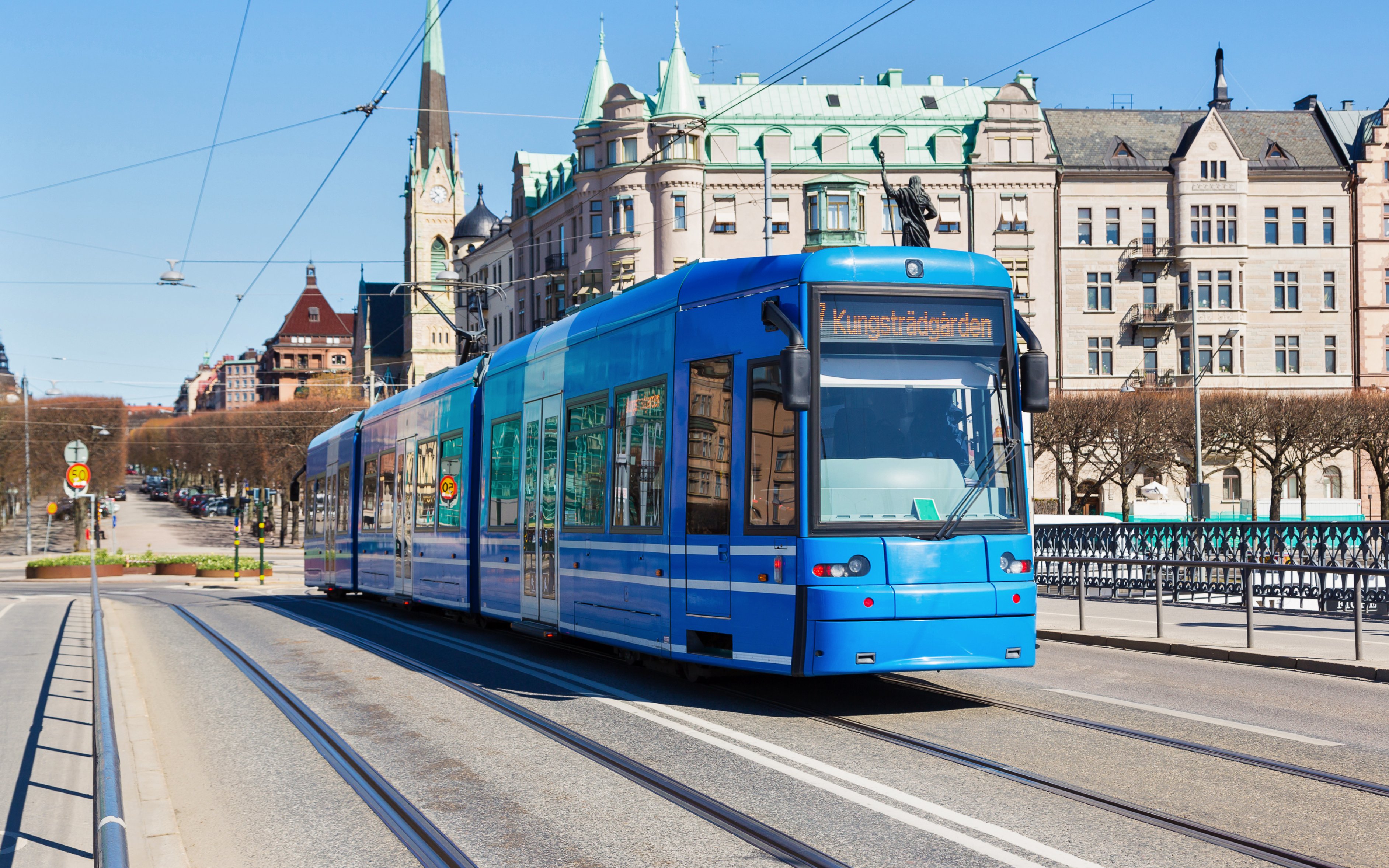 Modern tram on a street in Stockholm with historic buildings in the background.