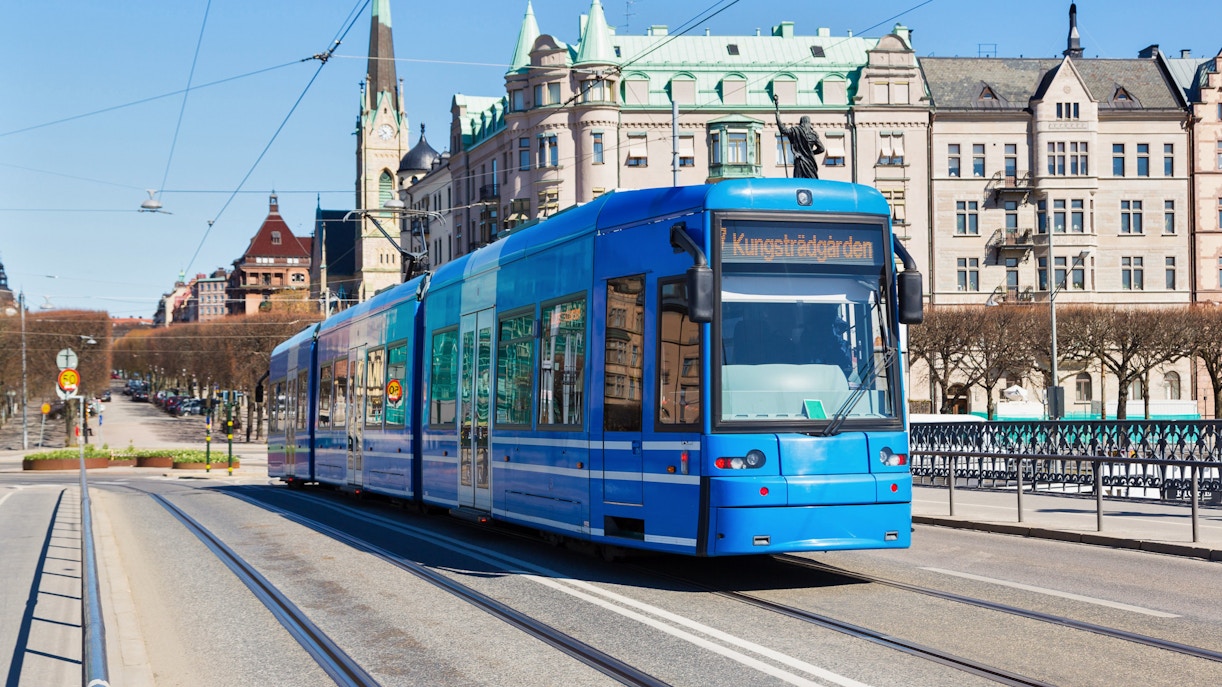 Modern tram on a street in Stockholm with historic buildings in the background.