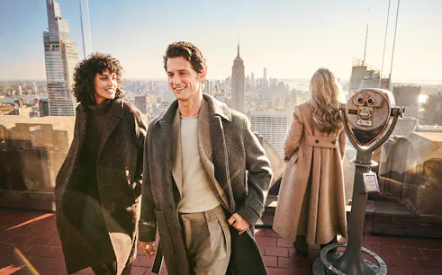 Visitors enjoying the view from Top of the Rock, New York, with the Empire State Building in the background.