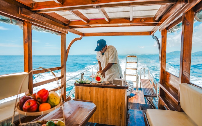 Longtail boat cruise in Krabi with a person preparing fresh fruit refreshments.