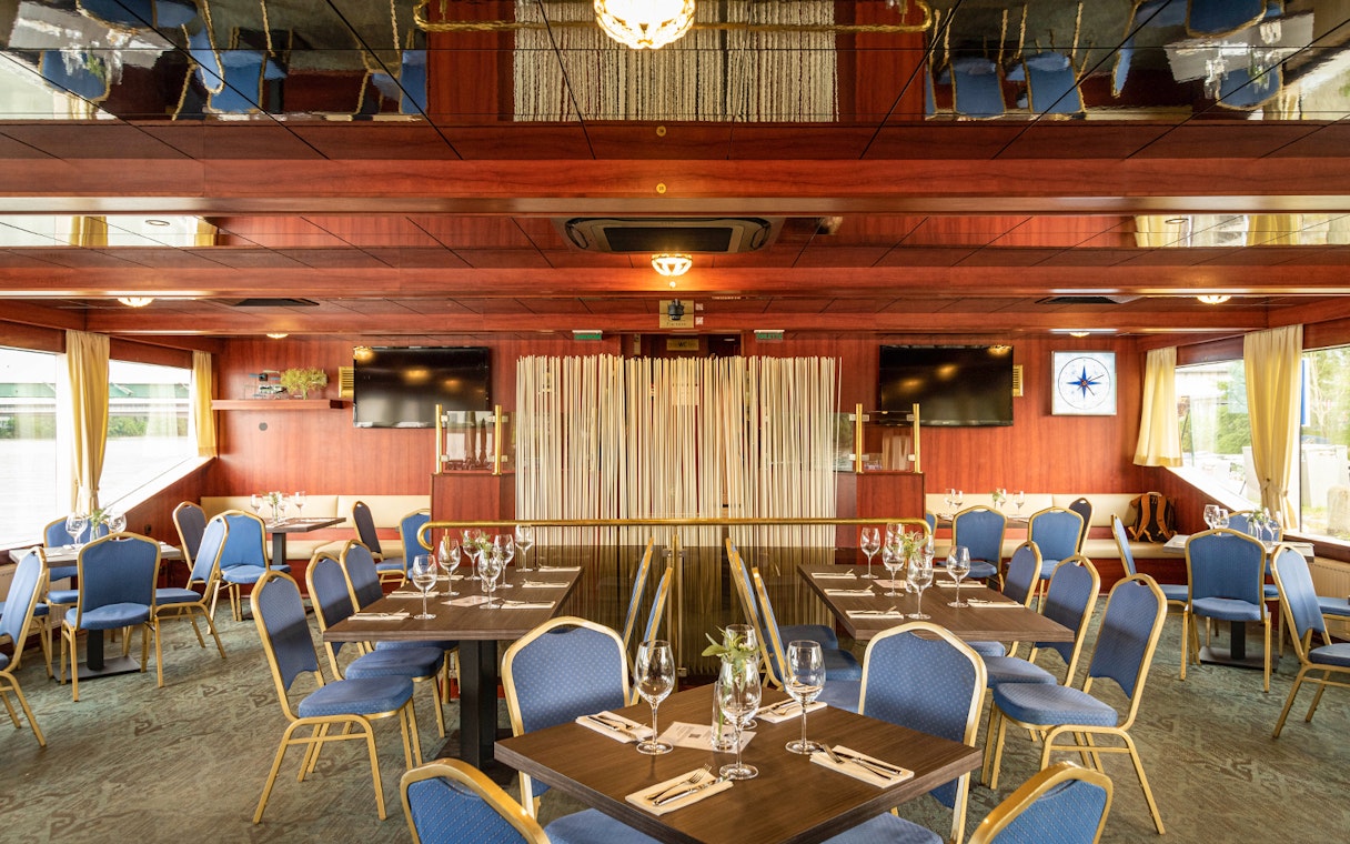 Interior of a cruise dining area with set tables and blue chairs on the Dürnstein and Wachau tour.