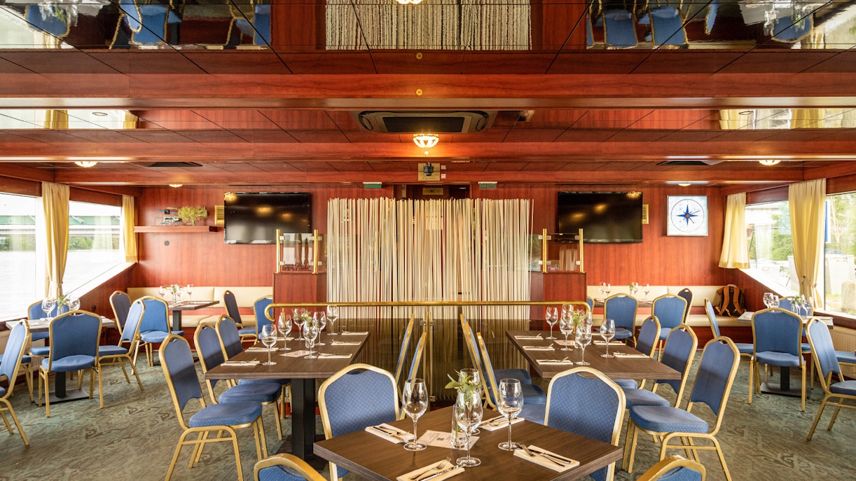 Interior of a cruise dining area with set tables and blue chairs on the Dürnstein and Wachau tour.