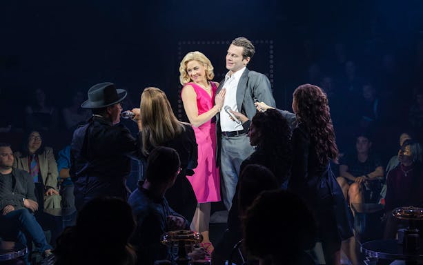 Performers on stage during a live theater show with audience in the background.