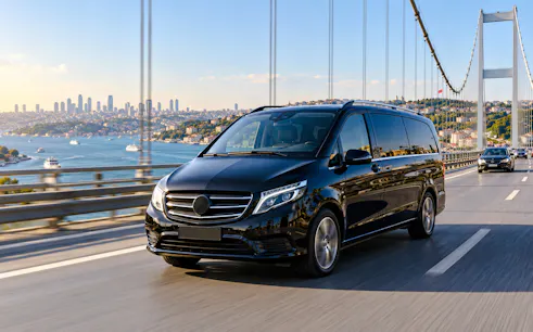 Private transfer van crossing Bosphorus Bridge, Istanbul, with city skyline in background.