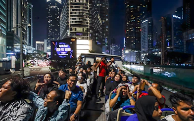 Tourists on Kuala Lumpur night bus tour viewing city skyline.