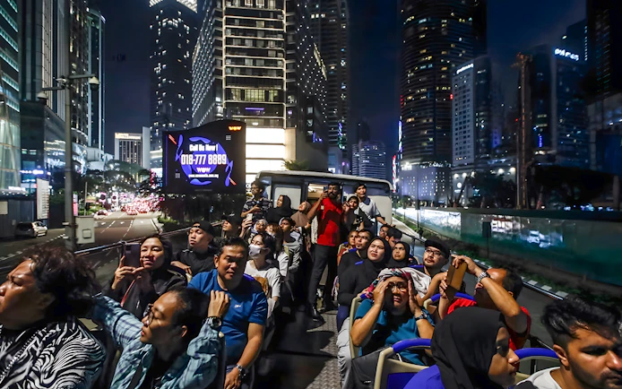 Tourists on Kuala Lumpur night bus tour viewing city skyline.