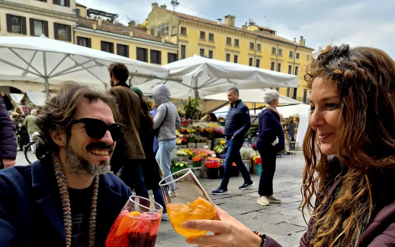 People enjoying drinks at Padova market during a food tour with flowers in the background.