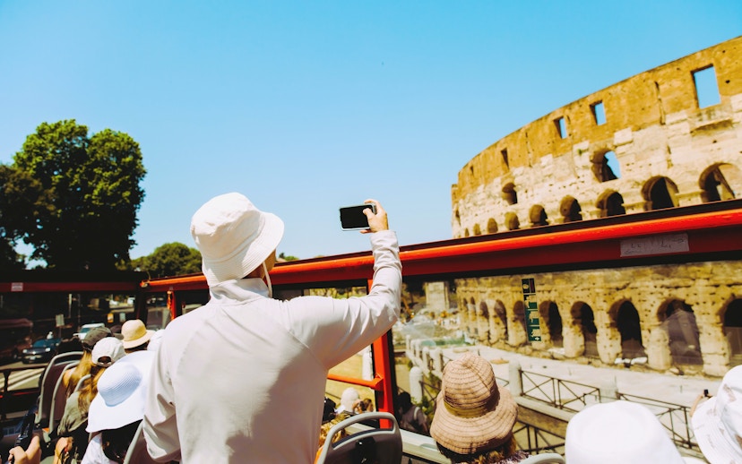 Tourists on HOHO bus tour capturing the Colosseum in Rome.