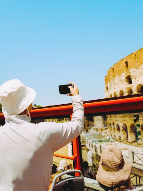 Tourists on HOHO bus tour capturing the Colosseum in Rome.