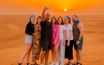 Group taking selfie during Abu Dhabi desert safari at sunset.