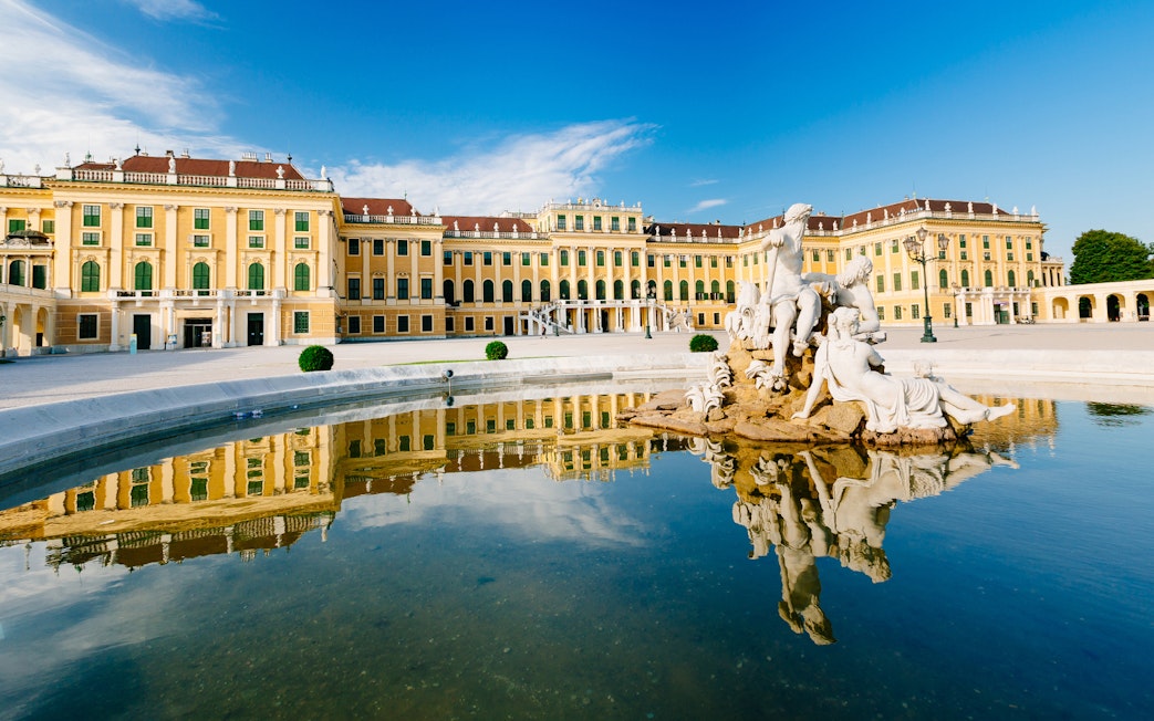 Schönbrunn Palace with Neptune Fountain in Vienna, Austria, reflecting in water.