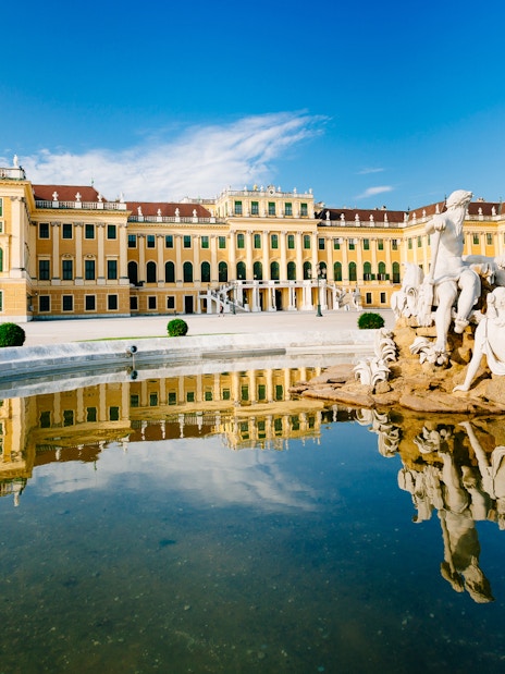 Schönbrunn Palace with Neptune Fountain in Vienna, Austria, reflecting in water.