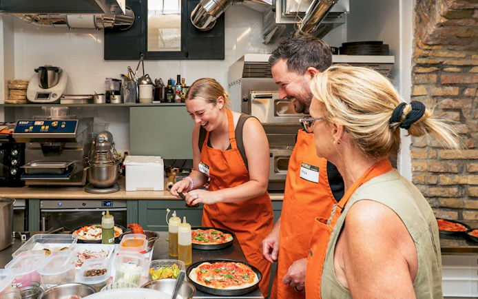 People in orange aprons making pizza in a cooking class.