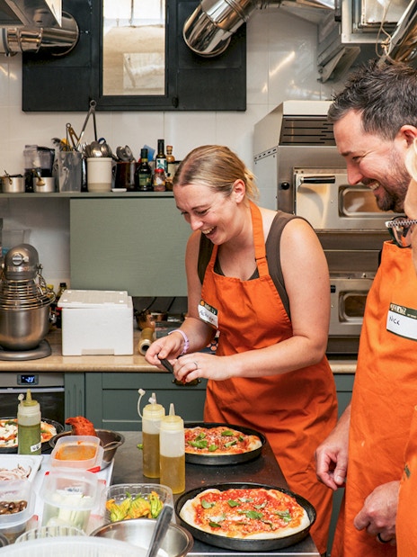 People in orange aprons making pizza in a cooking class.
