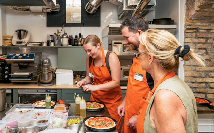 People in orange aprons making pizza in a cooking class.