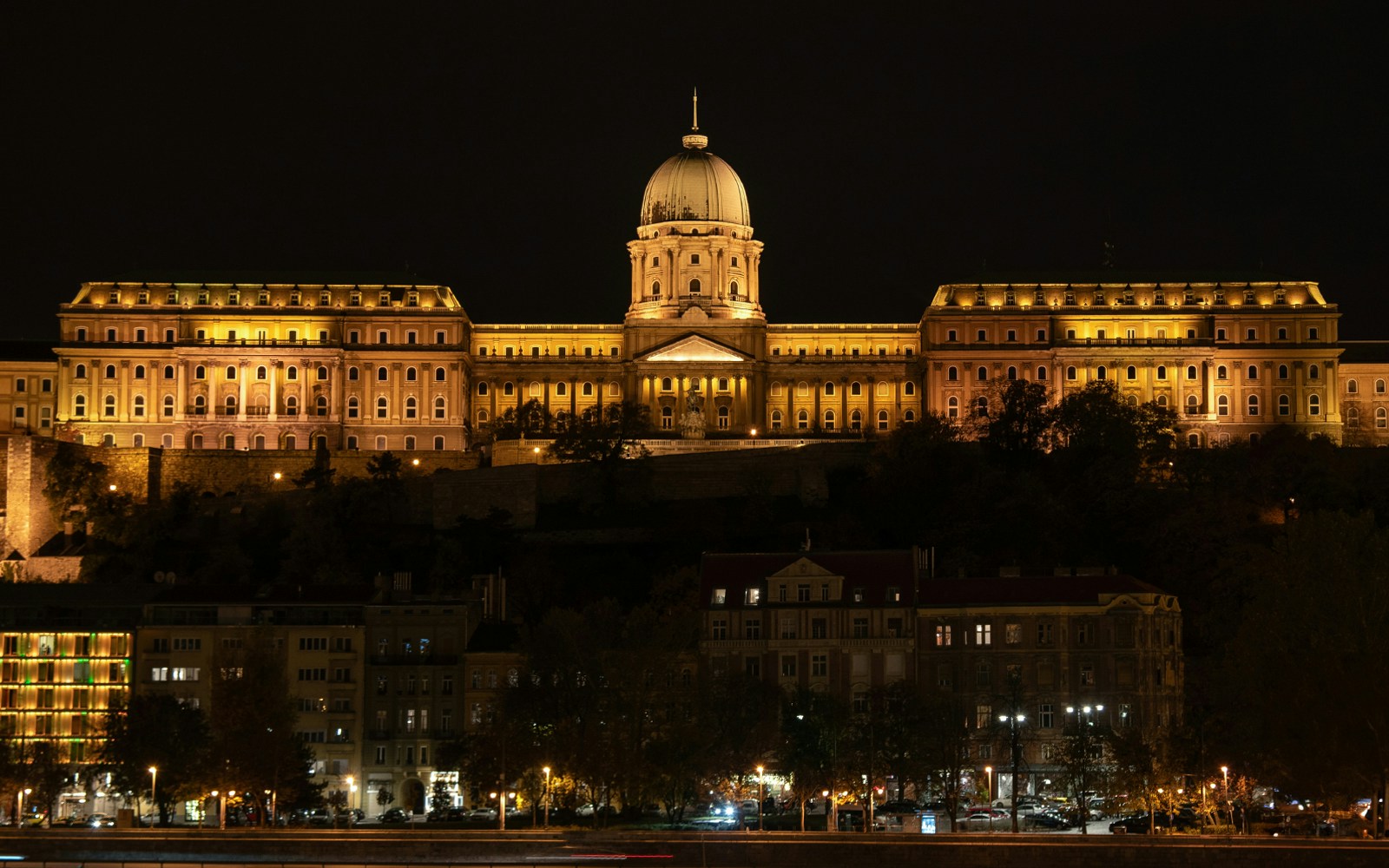 Buda Castle illuminated at night in Budapest, Hungary, with city lights in the background.