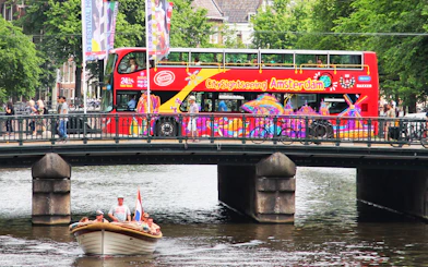 Amsterdam sightseeing bus on bridge over canal with boat below.
