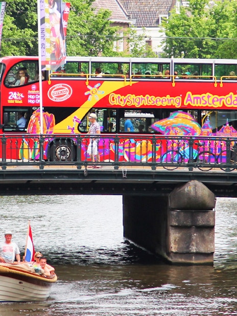 Amsterdam sightseeing bus on bridge over canal with boat below.