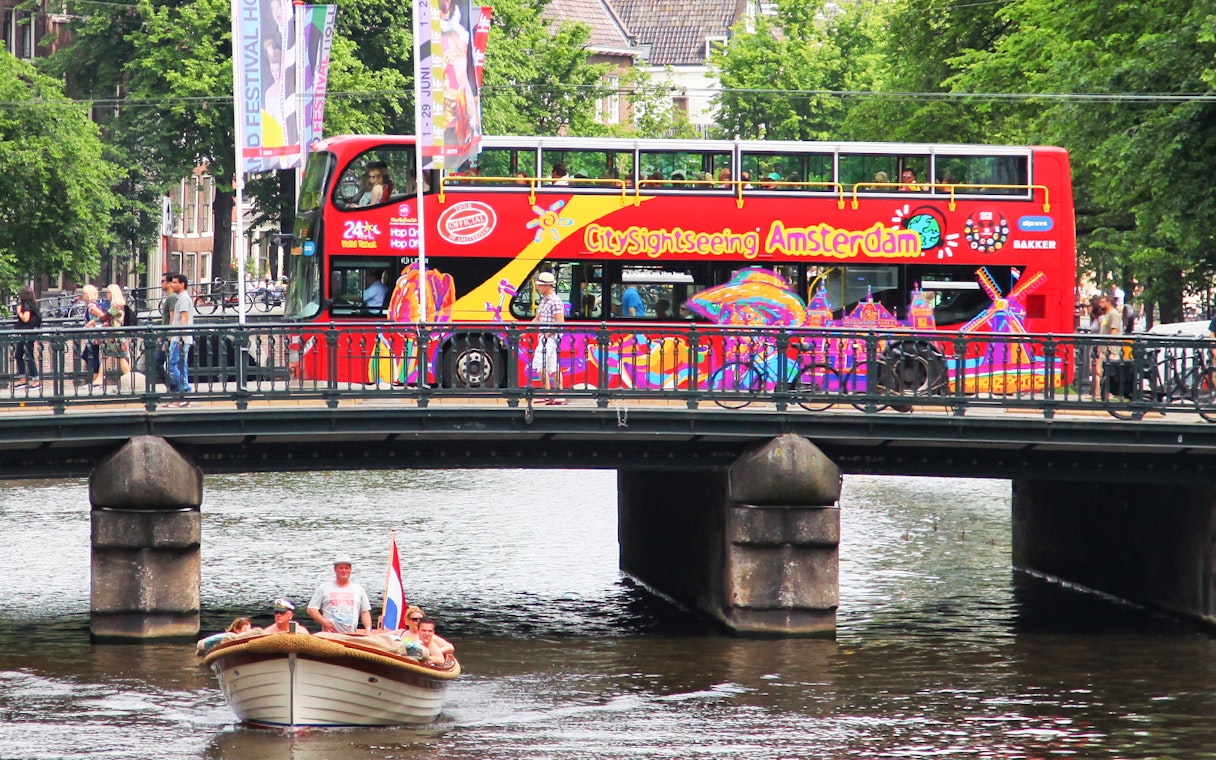 Amsterdam sightseeing bus on bridge over canal with boat below.