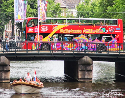 Amsterdam cityscape with iconic canal houses and a red Hop-On Hop-Off bus.
