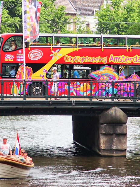 Amsterdam sightseeing bus on bridge over canal with boat below.