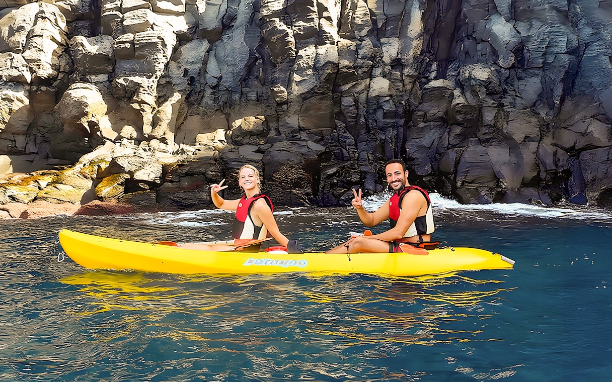 Tourists kayaking near rocky cliffs in Tenerife waters.