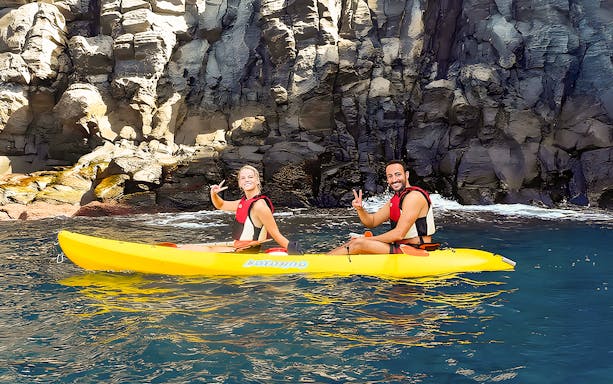 Tourists kayaking near rocky cliffs in Tenerife waters.