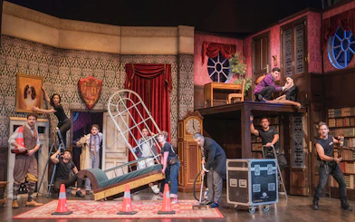 Theater cast performing a chaotic scene in "La Función Que Sale Mal" with props and set pieces.