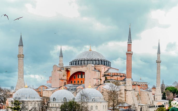 Hagia Sophia in Istanbul with its iconic domes and minarets under a cloudy sky.