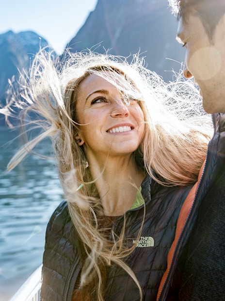 Couple enjoying a cruise on Milford Sound with mountains in the background.