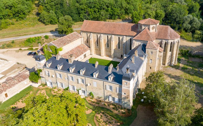 Aerial view of Beaulieu-en-Rouergue Abbey surrounded by lush greenery in France.