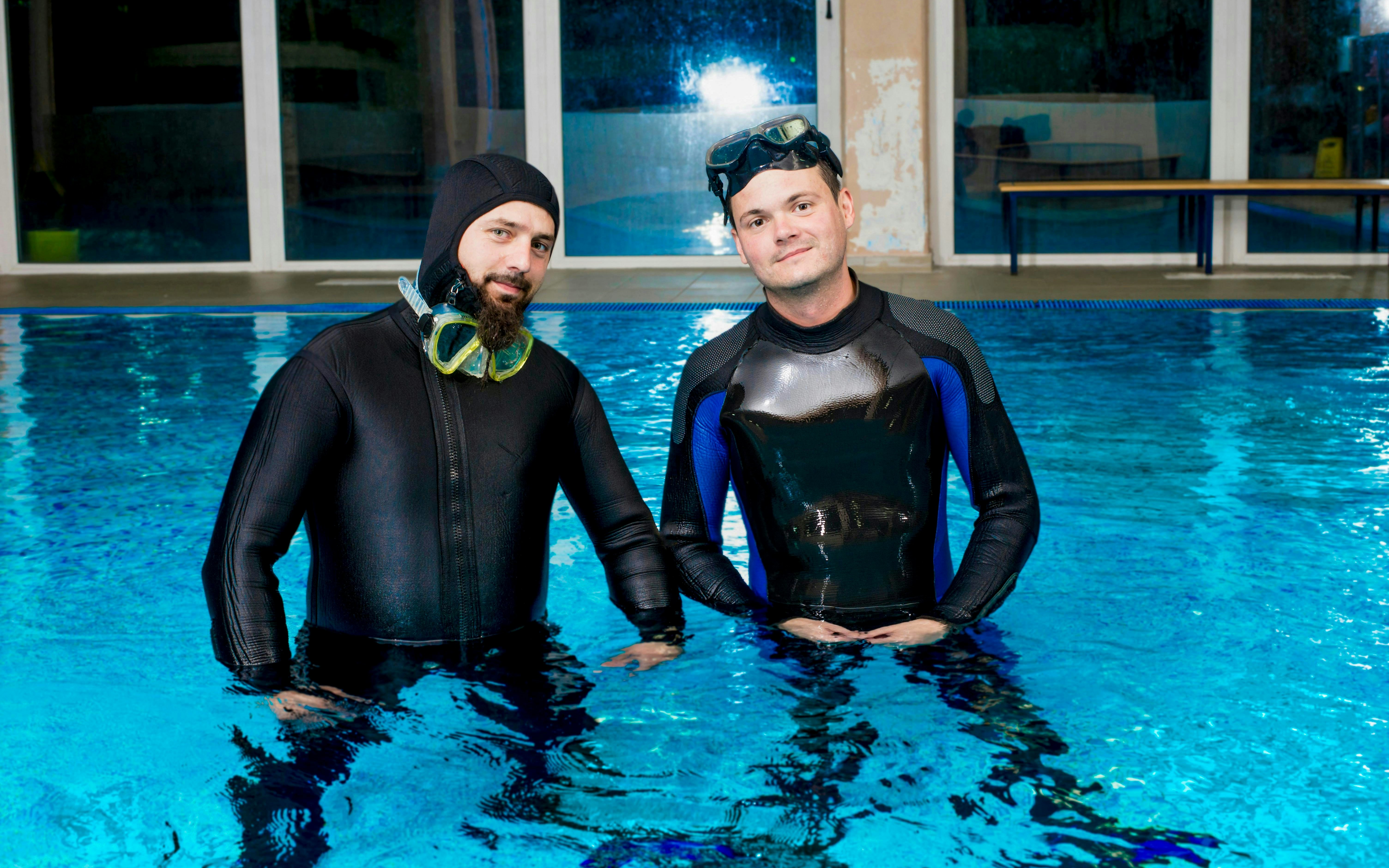 Visitor and trainer in scuba winter wetsuits standing in a pool during briefing.