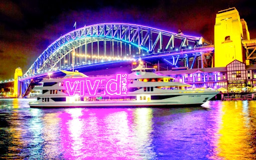 Sydney Harbour Bridge illuminated during Vivid Sydney light show with cruise ship in foreground.