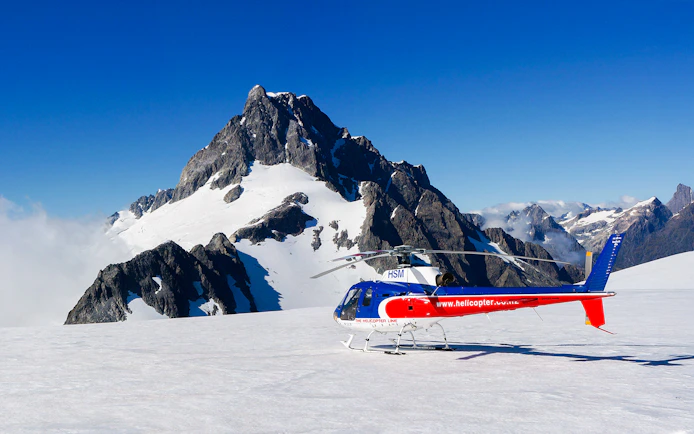 Helicopter on glacier with mountain backdrop, Milford Sound FlyCruiseHeli Tour.