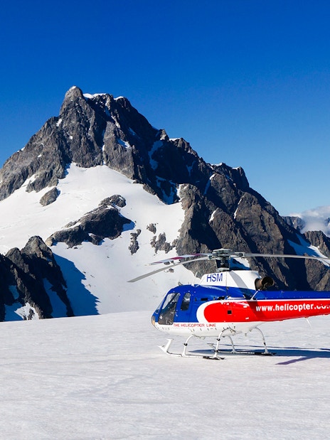 Helicopter on glacier with mountain backdrop, Milford Sound FlyCruiseHeli Tour.