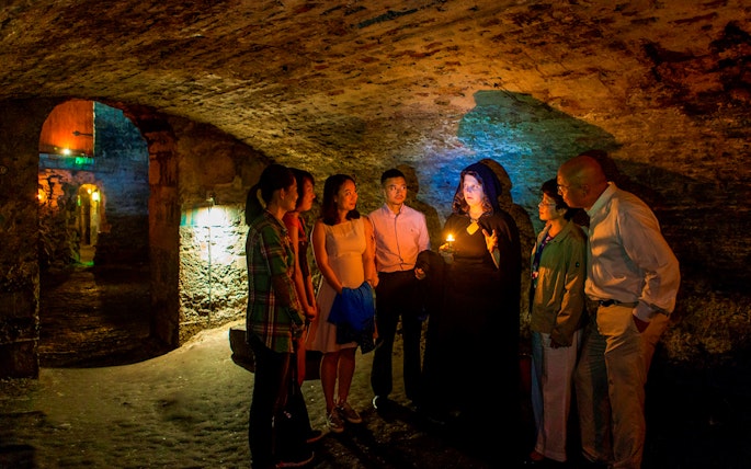 Group on Edinburgh ghost tour in underground vaults with guide holding candle.