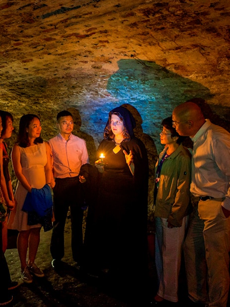Group on Edinburgh ghost tour in underground vaults with guide holding candle.