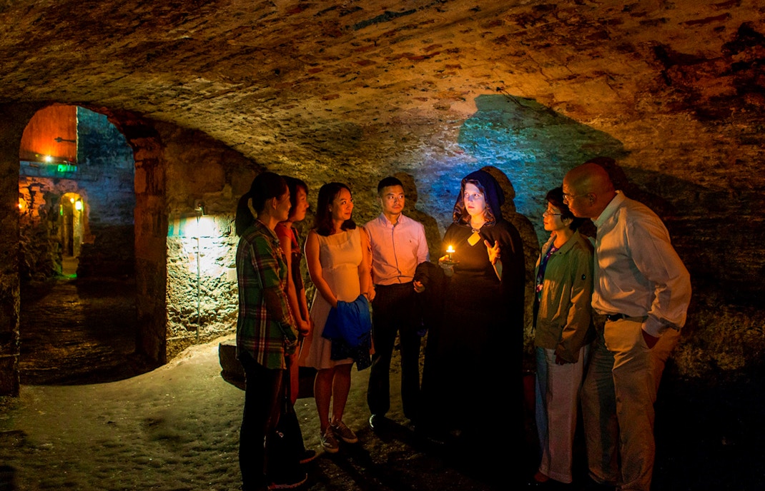 Group on Edinburgh ghost tour in underground vaults with guide holding candle.